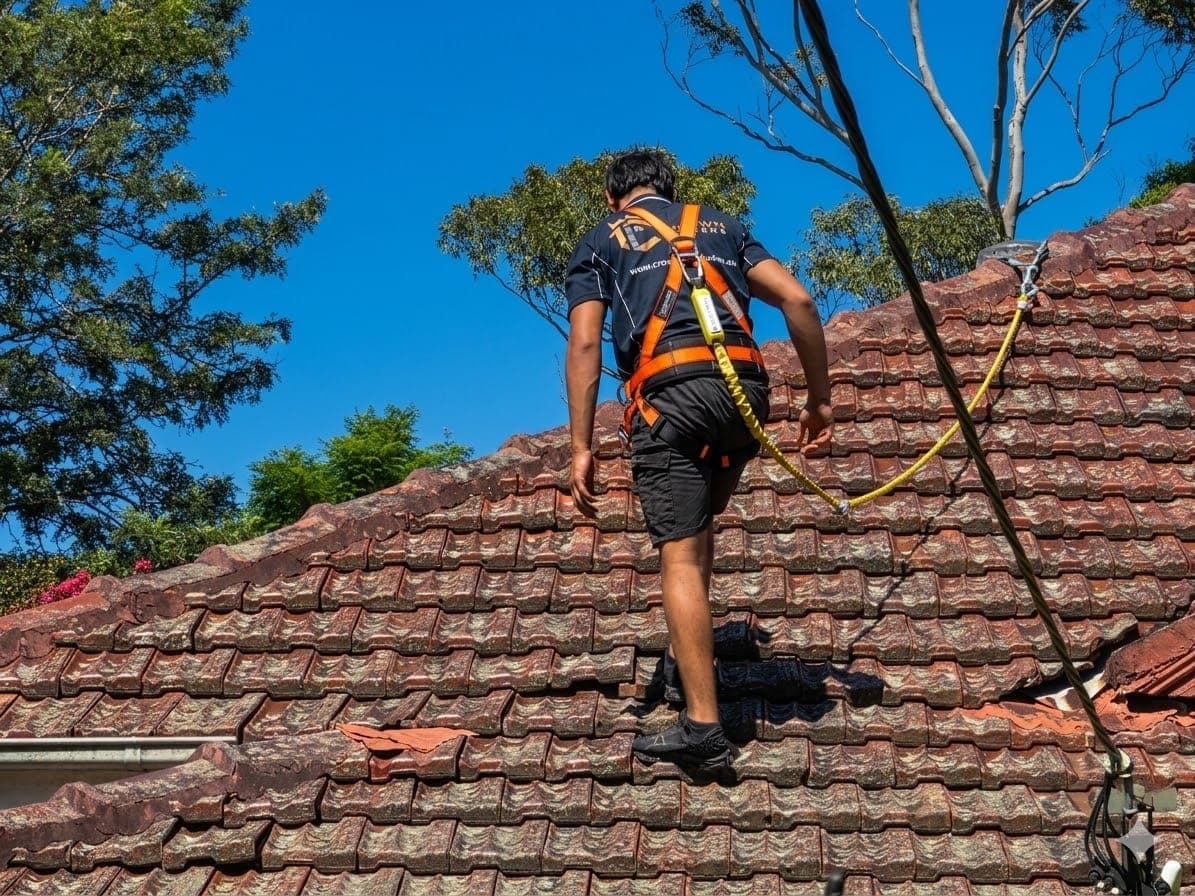 Licensed Crown Roofers roofer with safety harness on terracotta tile roof Sydney